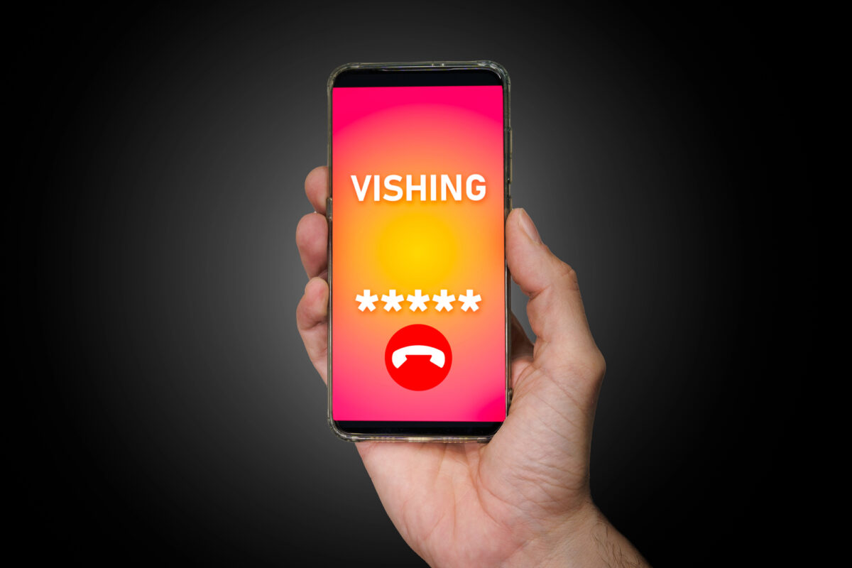 Main tenant un smartphone qui affiche un appel de vishing, un code masqué et le bouton pour raccrocher