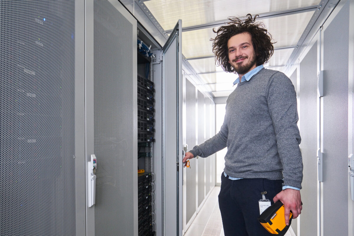 Technicien souriant ouvrant une baie de serveurs dans un datacenter, métier d'administrateur systèmes et réseaux